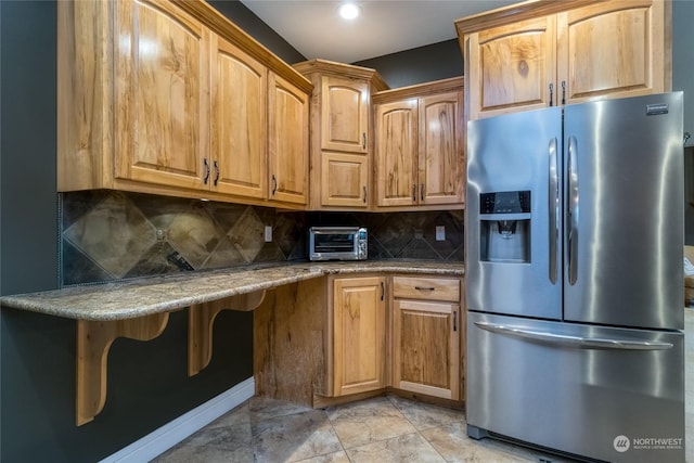 kitchen featuring tasteful backsplash, stone counters, stainless steel fridge, and light tile patterned floors