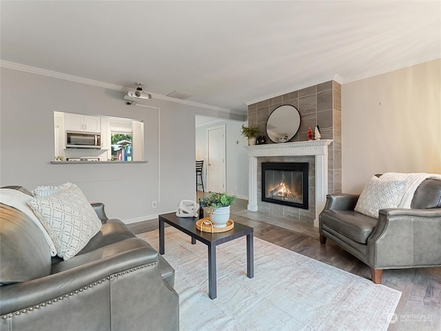 living room with a tile fireplace, crown molding, and hardwood / wood-style floors