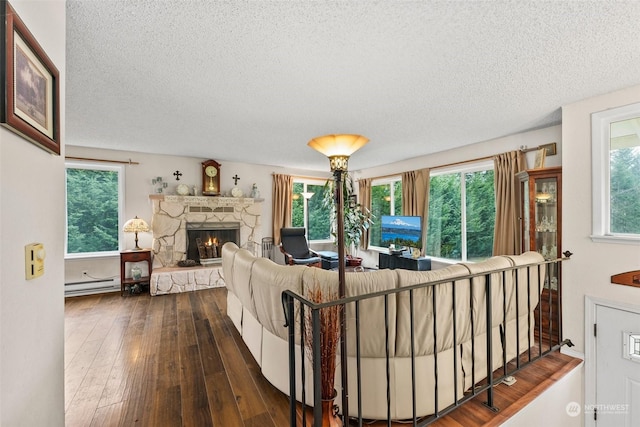 living room with dark wood-type flooring, a stone fireplace, a wealth of natural light, and a baseboard heating unit