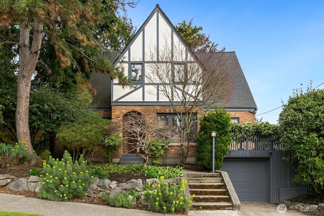 tudor-style house featuring brick siding, stucco siding, a shingled roof, and a garage