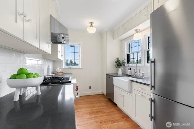 kitchen featuring a sink, decorative backsplash, stainless steel appliances, wall chimney exhaust hood, and light wood-type flooring