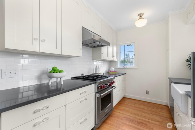 kitchen with decorative backsplash, stainless steel stove, dark countertops, and under cabinet range hood