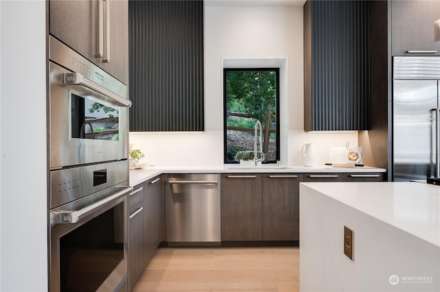 kitchen with stainless steel appliances, sink, and light hardwood / wood-style flooring