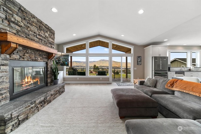 living room with a mountain view, a healthy amount of sunlight, a stone fireplace, and light colored carpet