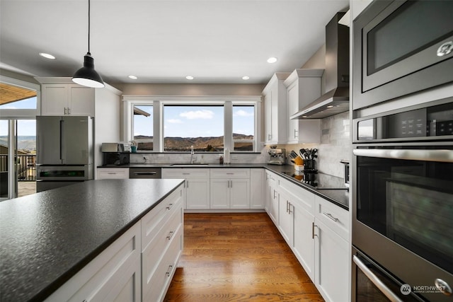 kitchen with white cabinets, wall chimney exhaust hood, decorative light fixtures, dark hardwood / wood-style flooring, and stainless steel appliances