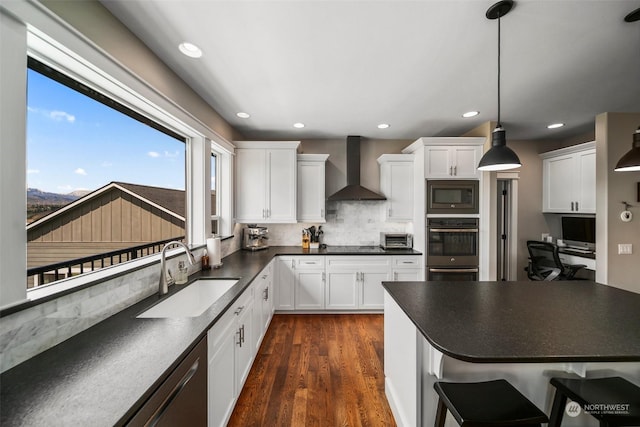 kitchen featuring white cabinetry, built in microwave, sink, hanging light fixtures, and wall chimney range hood