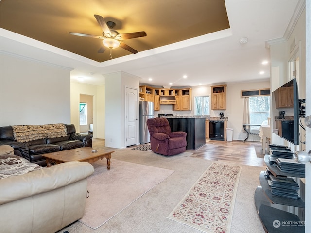 living room with ceiling fan, ornamental molding, a tray ceiling, and light hardwood / wood-style flooring