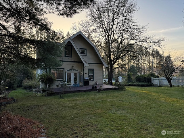 back house at dusk featuring a yard, a wooden deck, and french doors