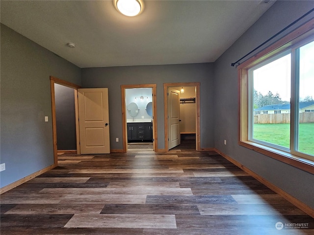 unfurnished bedroom featuring a walk in closet, ensuite bath, a closet, and dark wood-type flooring