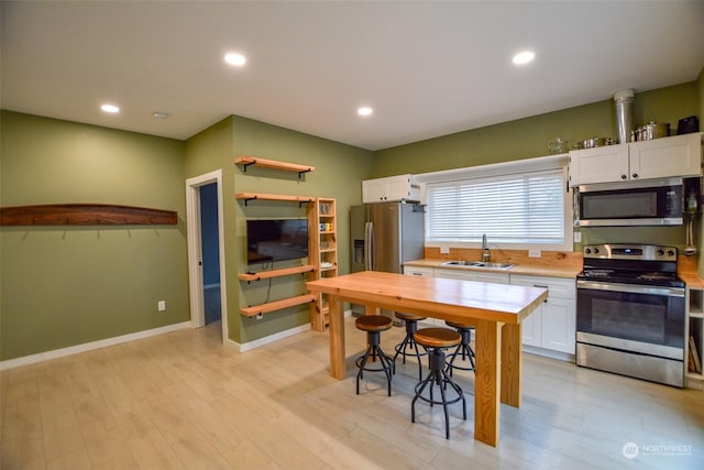 kitchen with appliances with stainless steel finishes, light wood-type flooring, white cabinetry, and sink