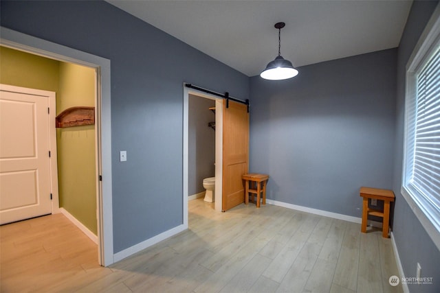 unfurnished bedroom with a barn door, ensuite bath, and light hardwood / wood-style floors