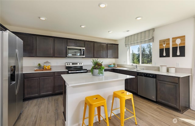 kitchen featuring dark brown cabinetry, a center island, a breakfast bar, appliances with stainless steel finishes, and light wood-type flooring