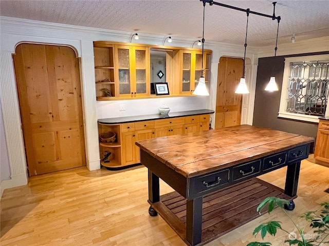 kitchen with a textured ceiling, crown molding, light wood-type flooring, and hanging light fixtures