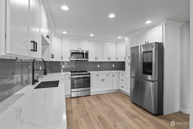 kitchen with appliances with stainless steel finishes, light stone counters, sink, light hardwood / wood-style floors, and white cabinetry