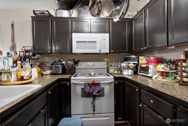 kitchen with white appliances, dark brown cabinetry, and dark stone countertops