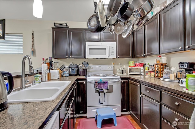 kitchen with light stone countertops, dark brown cabinetry, white appliances, and sink