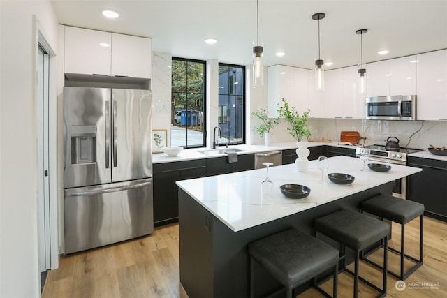 kitchen featuring a center island, light hardwood / wood-style flooring, pendant lighting, white cabinets, and appliances with stainless steel finishes