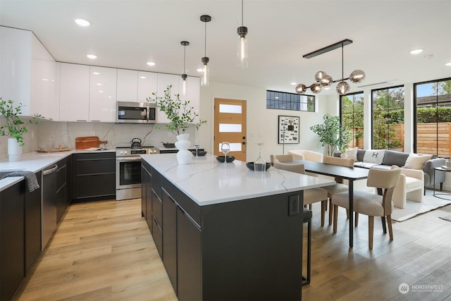 kitchen featuring light hardwood / wood-style flooring, a kitchen island, hanging light fixtures, and appliances with stainless steel finishes