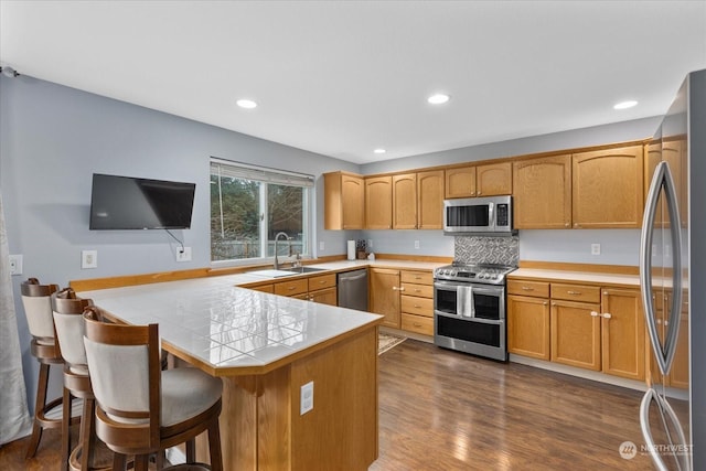 kitchen with sink, dark wood-type flooring, a kitchen breakfast bar, kitchen peninsula, and appliances with stainless steel finishes