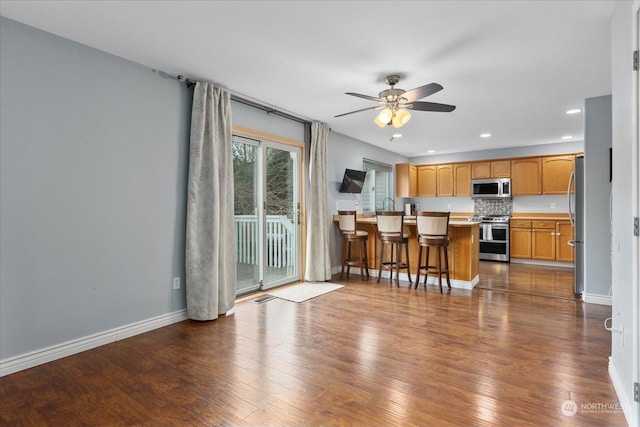 kitchen with appliances with stainless steel finishes, a kitchen breakfast bar, ceiling fan, dark hardwood / wood-style floors, and a kitchen island