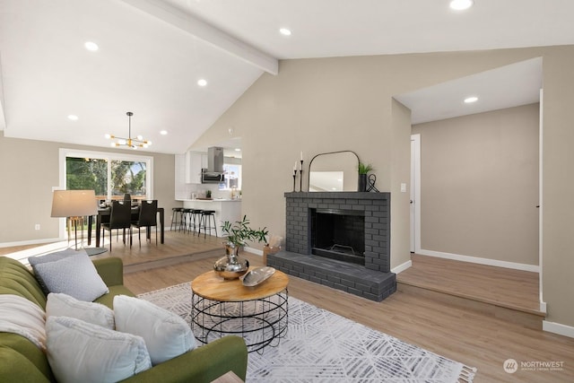 living room with a fireplace, lofted ceiling with beams, an inviting chandelier, and light hardwood / wood-style flooring