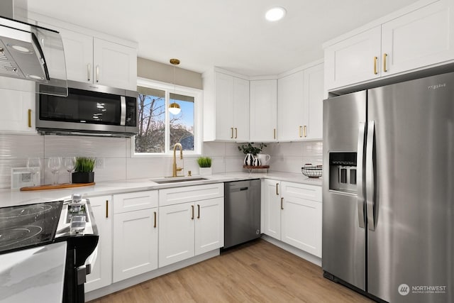 kitchen featuring white cabinets, sink, appliances with stainless steel finishes, decorative light fixtures, and light hardwood / wood-style floors