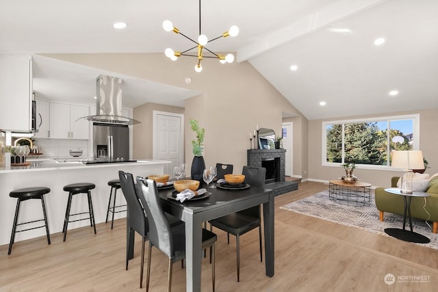 dining room with vaulted ceiling with beams, a fireplace, a chandelier, and light wood-type flooring