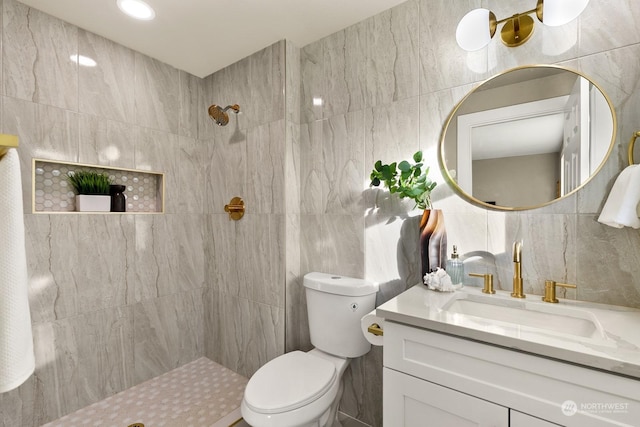 bathroom featuring a tile shower, vanity, tile walls, and toilet