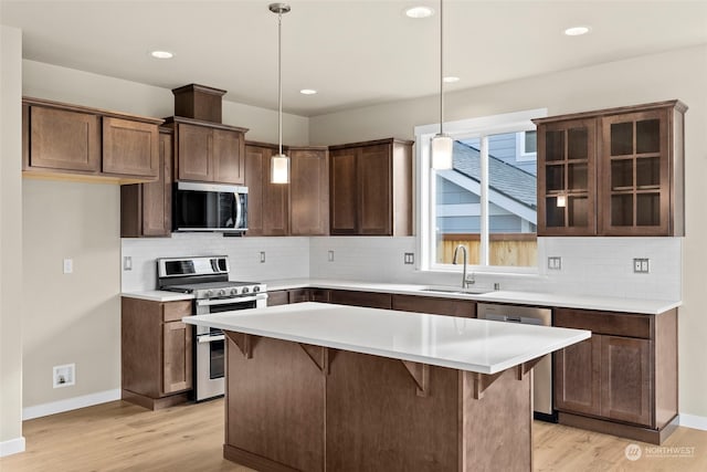 kitchen featuring a kitchen island, appliances with stainless steel finishes, sink, hanging light fixtures, and light hardwood / wood-style flooring