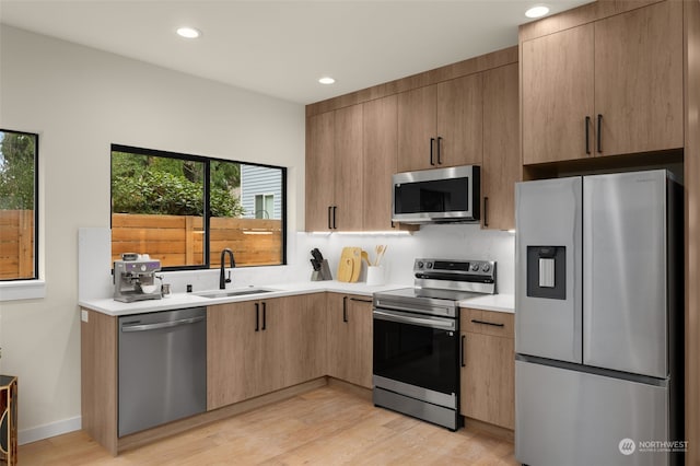 kitchen with decorative backsplash, appliances with stainless steel finishes, light wood-type flooring, sink, and light brown cabinets