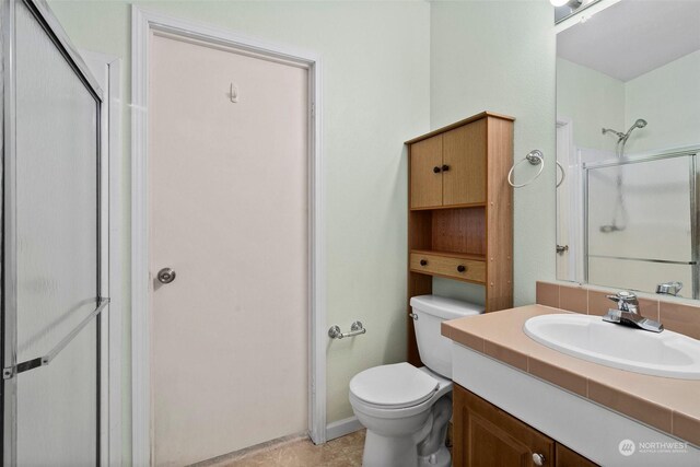 bathroom featuring tile patterned flooring, vanity, toilet, and a shower with shower door