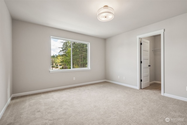 unfurnished bedroom with light colored carpet, a walk in closet, and a closet