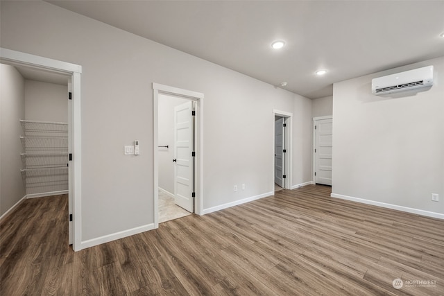 unfurnished bedroom with a wall mounted air conditioner, a walk in closet, hardwood / wood-style flooring, and ensuite bath