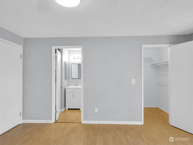 unfurnished bedroom featuring light wood-type flooring, a textured ceiling, connected bathroom, and a walk in closet