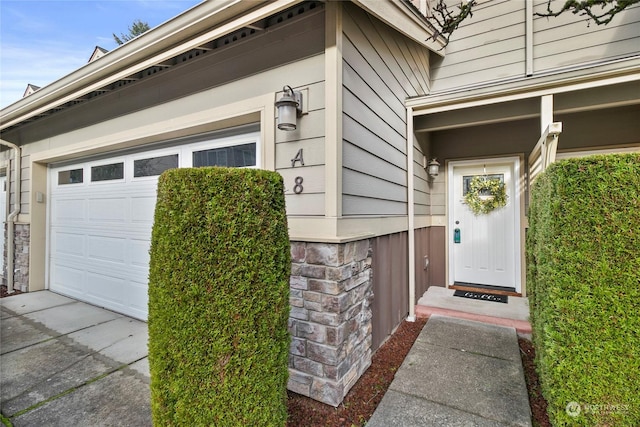 doorway to property with a garage, stone siding, and driveway