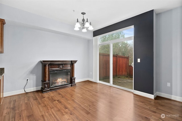 unfurnished living room with an inviting chandelier, wood finished floors, baseboards, and a lit fireplace