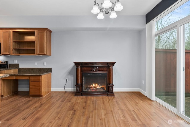 interior space featuring an inviting chandelier, light wood-style flooring, baseboards, and a warm lit fireplace