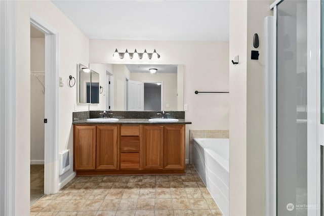 bathroom with a bath, visible vents, double vanity, and a sink