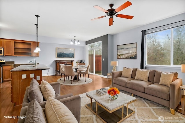 living area with baseboards, light wood-style floors, and ceiling fan with notable chandelier