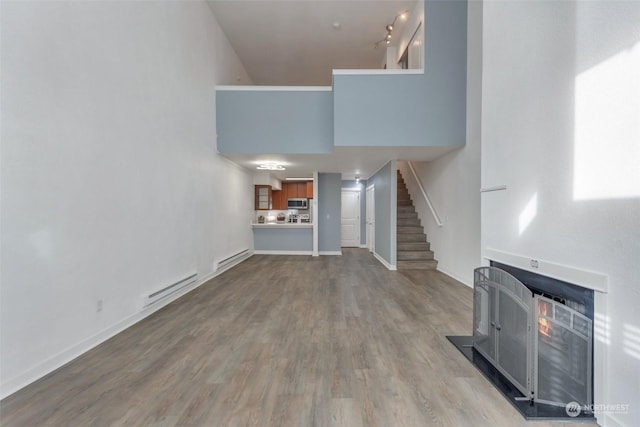 unfurnished living room with a towering ceiling, light hardwood / wood-style flooring, and a baseboard heating unit