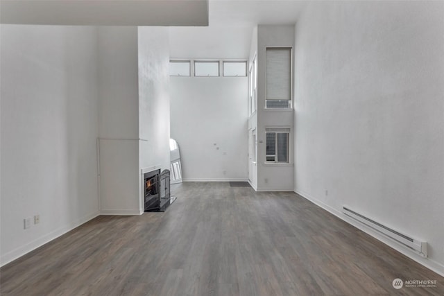 unfurnished living room with dark hardwood / wood-style flooring, a healthy amount of sunlight, a high ceiling, and baseboard heating