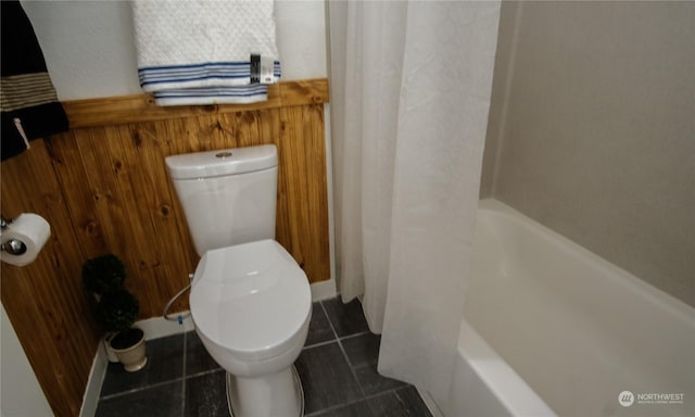 bathroom with toilet, tile patterned floors, wooden walls, and shower / bath combo