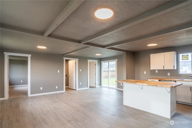 kitchen featuring a breakfast bar area, butcher block counters, white cabinetry, and light hardwood / wood-style flooring