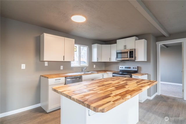 kitchen with wooden counters, light wood-type flooring, stainless steel appliances, sink, and white cabinets