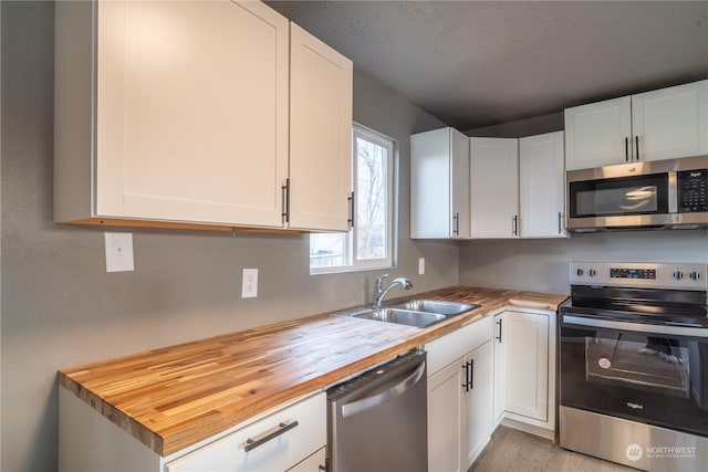 kitchen with butcher block counters, white cabinetry, and stainless steel appliances