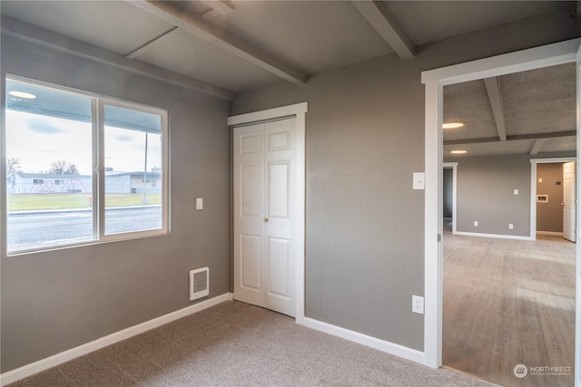 unfurnished bedroom featuring beamed ceiling, hardwood / wood-style flooring, and a closet