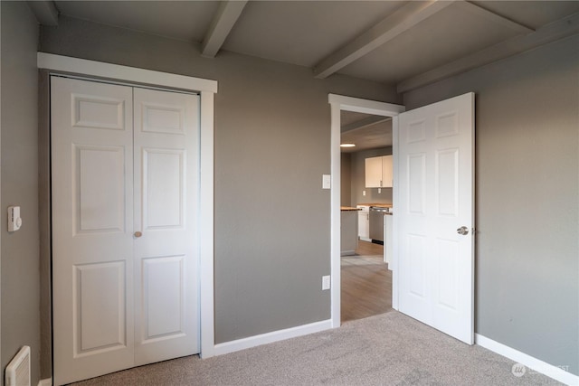 unfurnished bedroom featuring beam ceiling, light colored carpet, and a closet