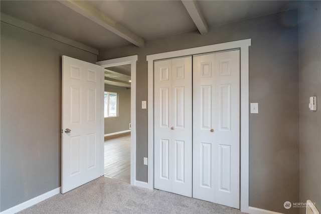 unfurnished bedroom with a closet, beamed ceiling, and light colored carpet