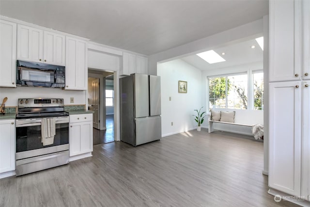 kitchen featuring white cabinets, appliances with stainless steel finishes, light wood-type flooring, and vaulted ceiling with skylight