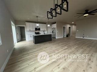 kitchen with pendant lighting, a kitchen island with sink, white cabinets, ceiling fan, and light hardwood / wood-style floors